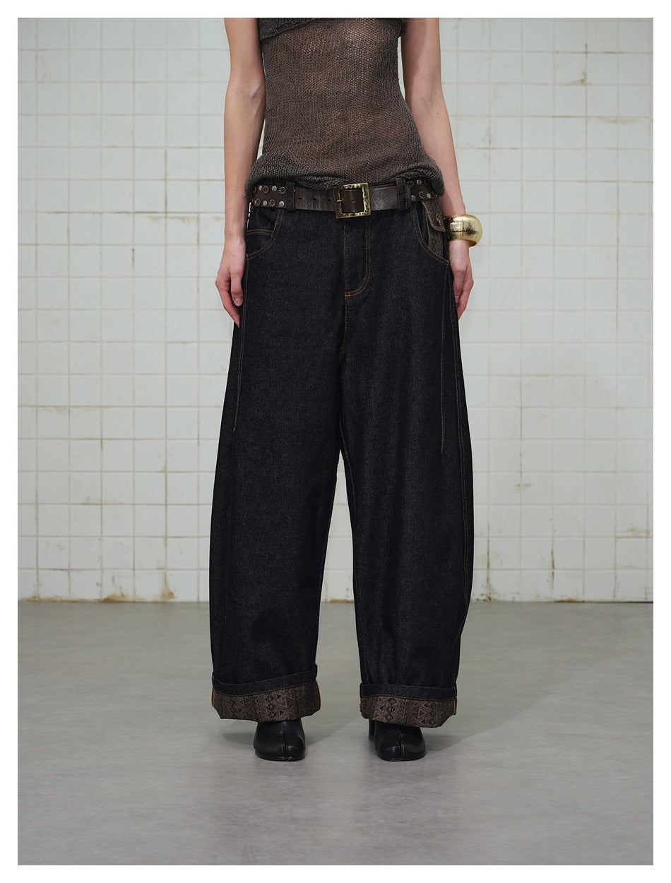 Cropped front view of a model wearing dark indigo wide-leg jeans with patterned turned-up cuffs.