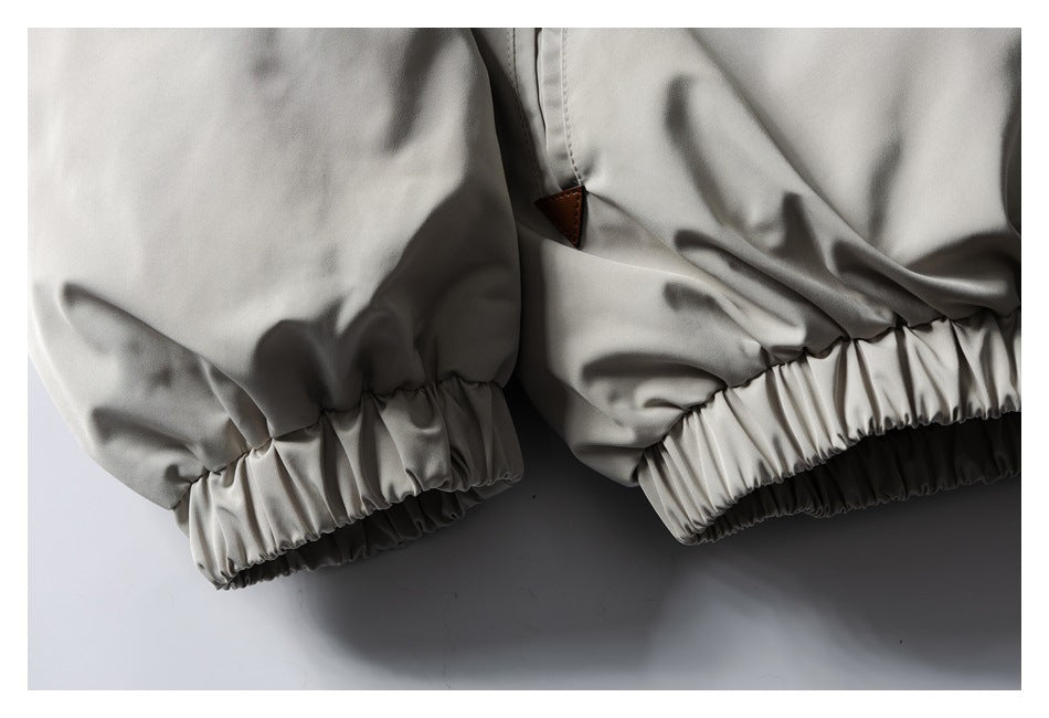 Close-up of a light gray jacket showing gathered elastic cuffs and a small brown triangular tab.