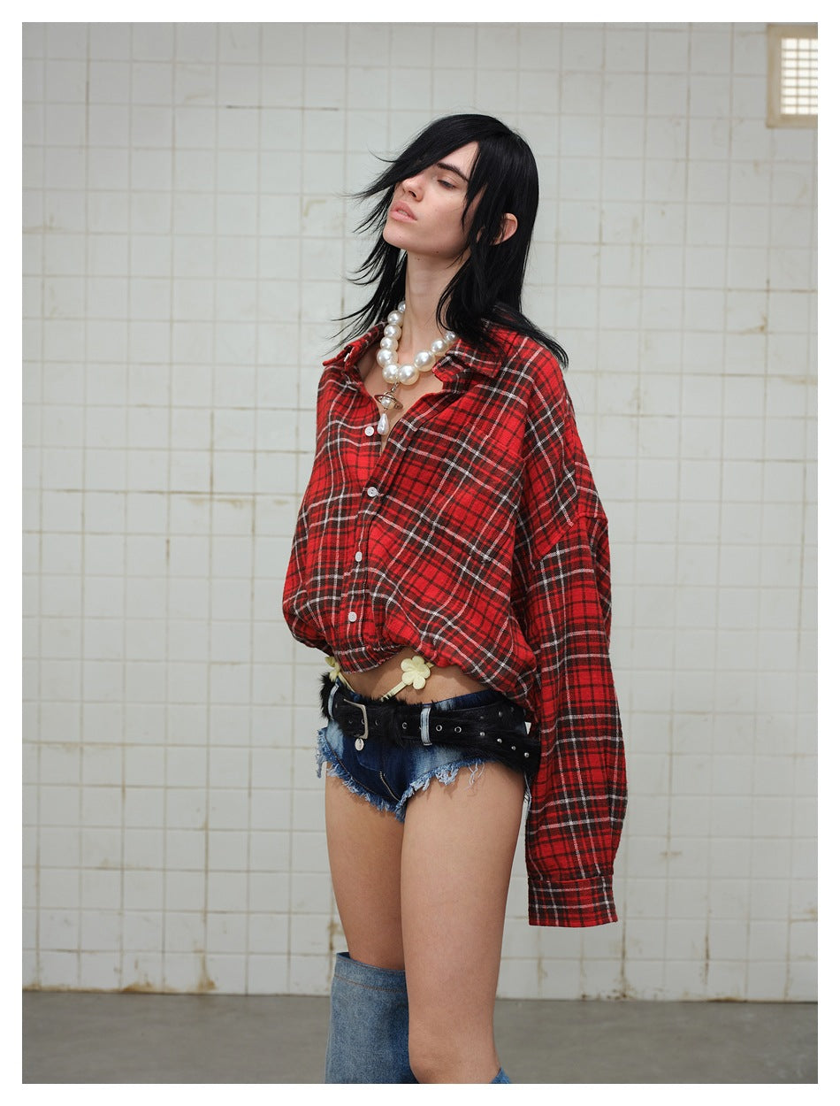 Side view of a model wearing an oversized red plaid button-up shirt and dark frayed denim shorts.