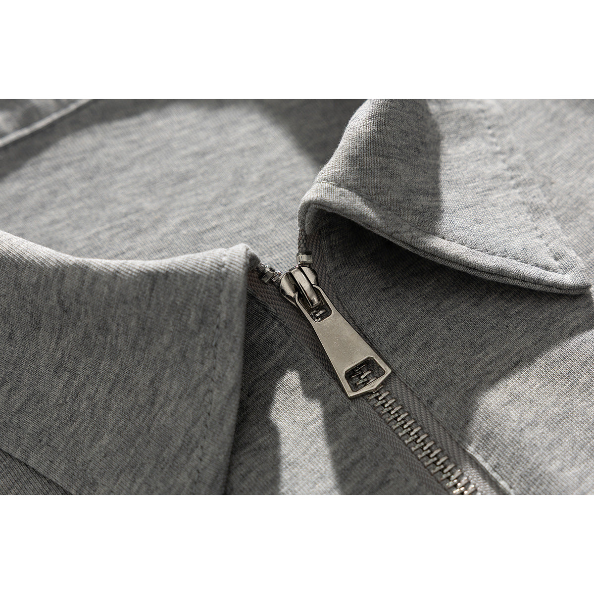 Close-up of a gray knit top showing its short metal zipper and collar edge.