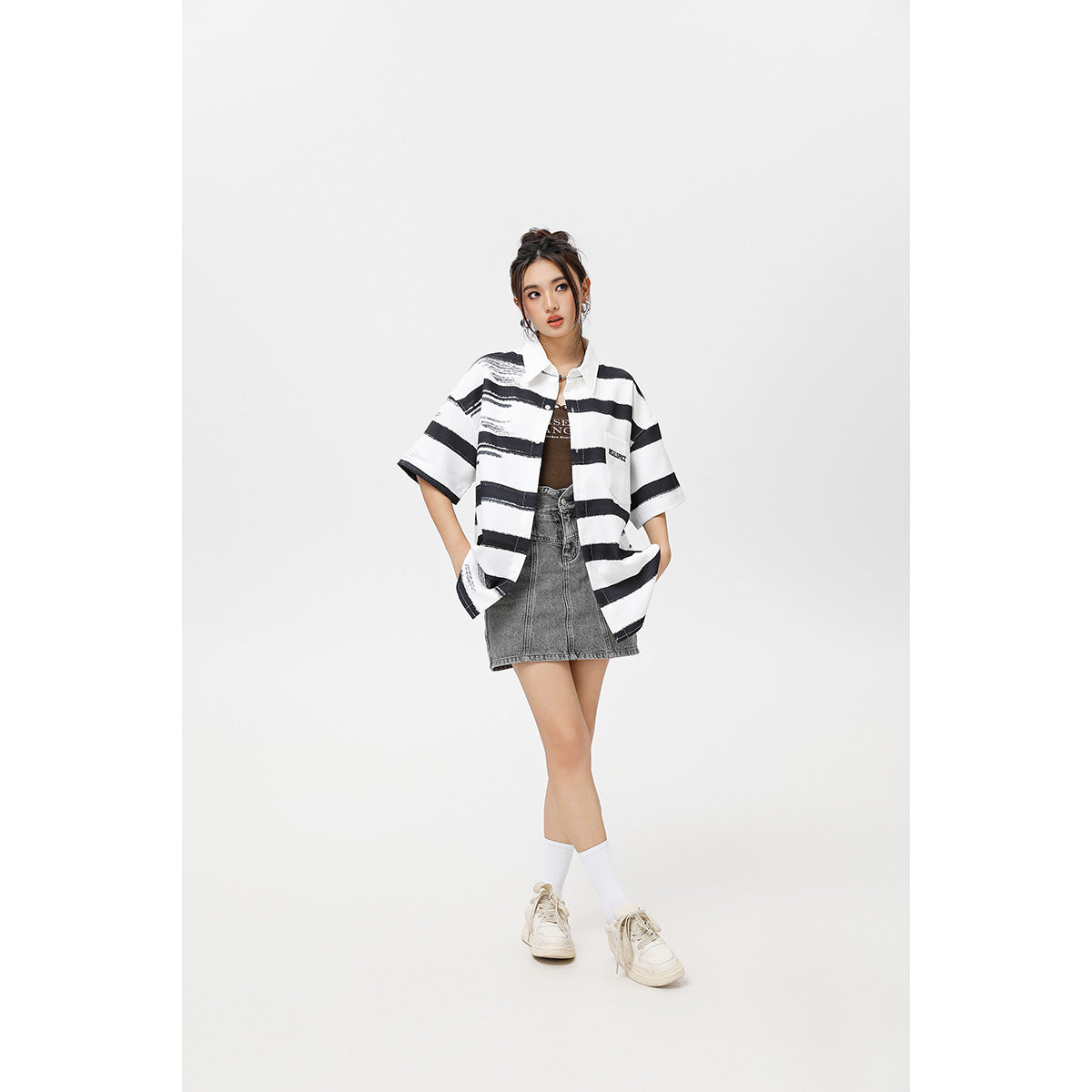 Model wearing an open oversized white shirt with black brushstroke stripes over a gray denim mini skirt.