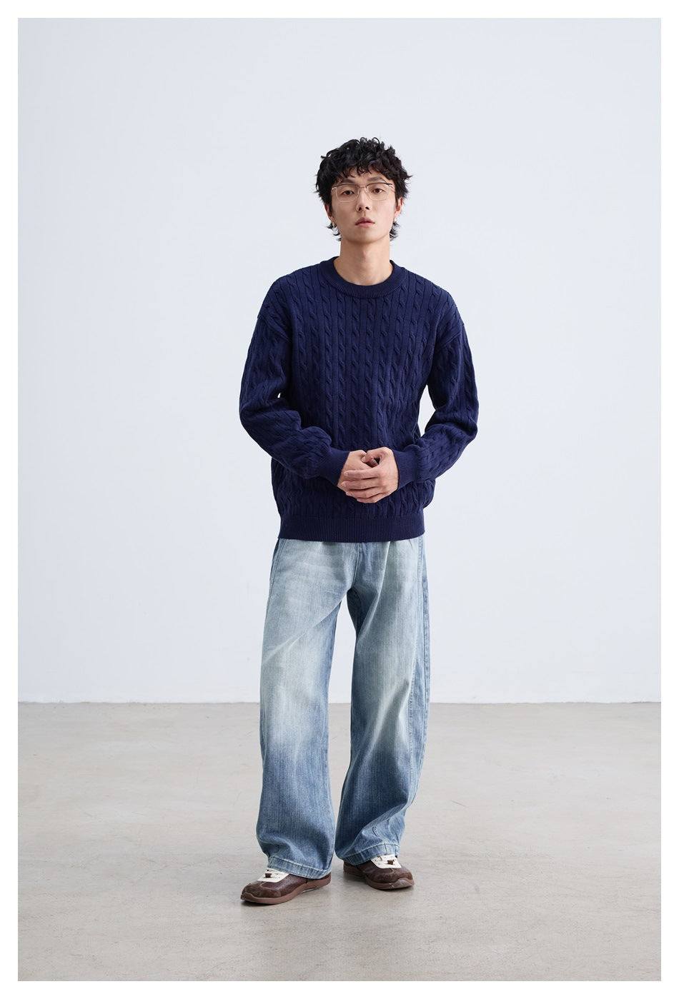 Model wearing a navy cable-knit crewneck sweater with light blue wide-leg jeans, shown standing front-facing.