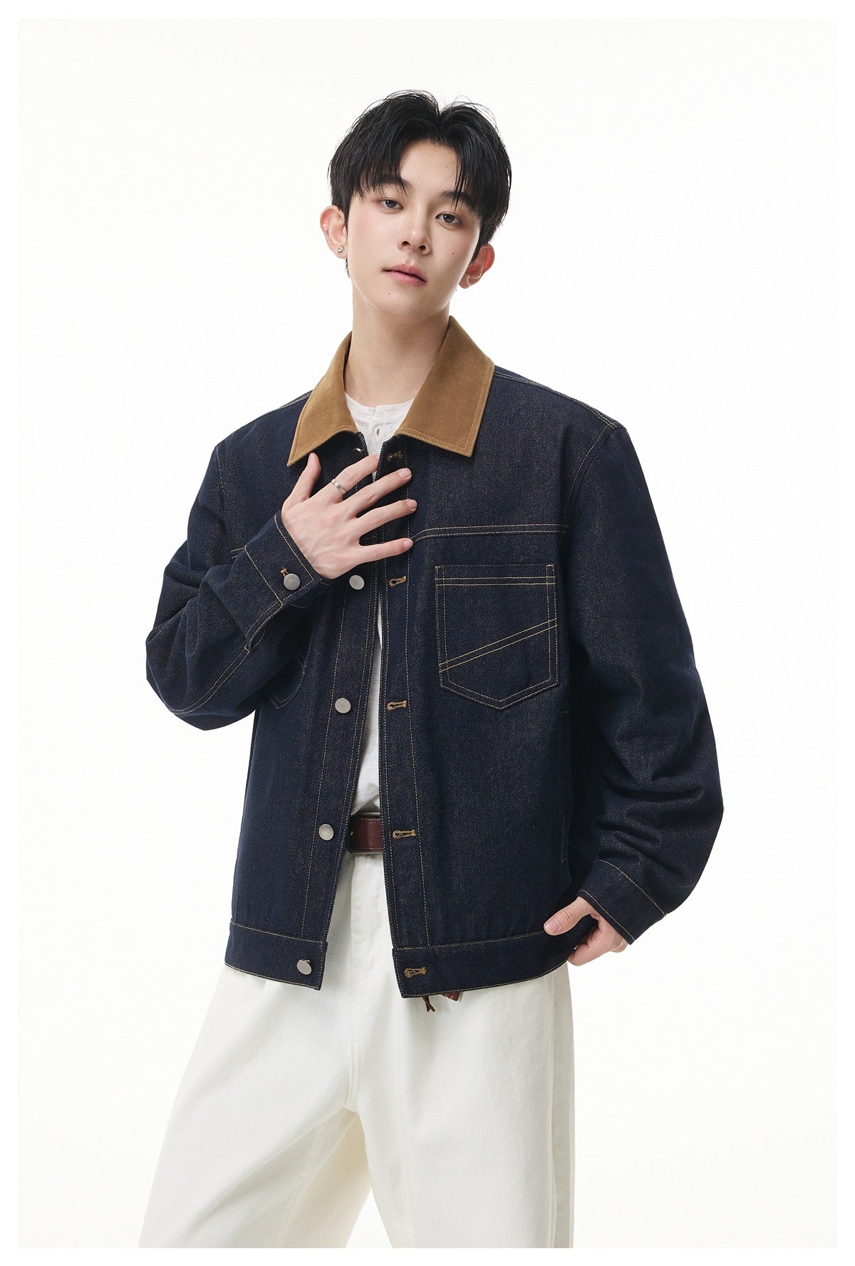 Model wearing a dark indigo denim jacket with a tan collar and contrast stitching, paired with white trousers.