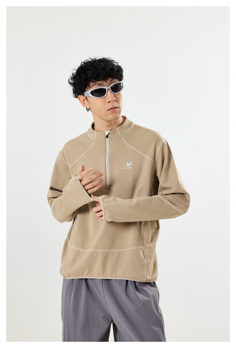 Close view of a man wearing a beige quarter-zip pullover with pale contrast seams and long sleeves with thumbholes.