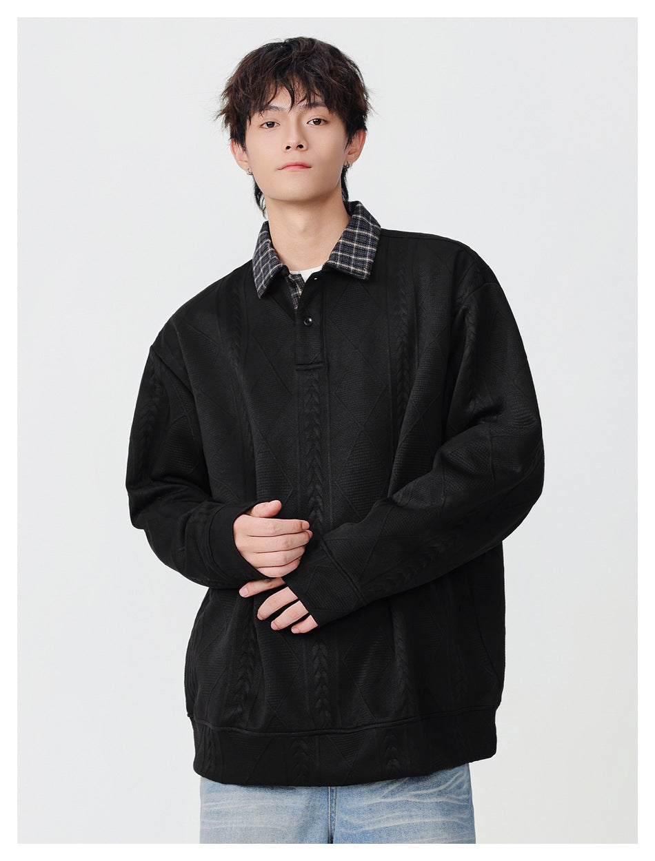 Front view of a model in an oversized black pullover with a plaid collar and raised cable and diamond patterns.