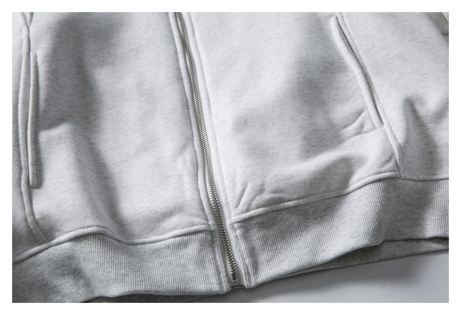 Close-up of a light gray zip-up hoodie showing the zipper, front pockets, and ribbed hem.