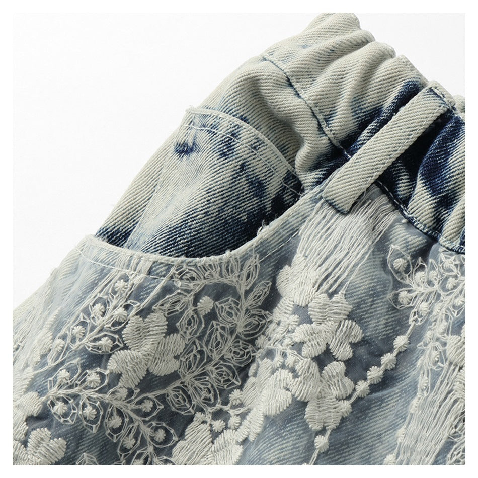 Close-up of white floral embroidery over washed blue denim, beside a pocket and belt loop.