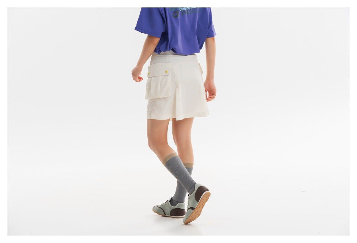 Rear three-quarter view of an ivory utility skort with a large flap pocket, modeled with a purple T-shirt.