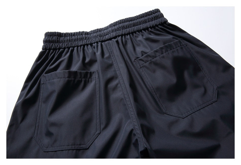 Cropped rear view of dark trousers showing an elastic waistband and two patch pockets.