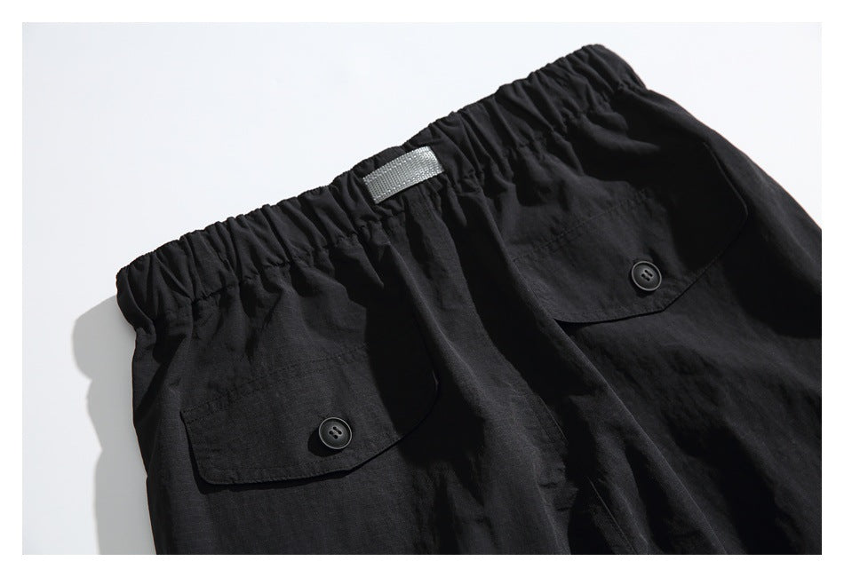 Close-up of black pants with an elastic waistband and two button-flap pockets.