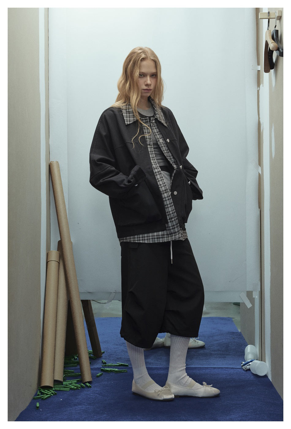 Model wearing a black oversized plaid-collar jacket with hands in the front pockets, over a plaid layer and gray top