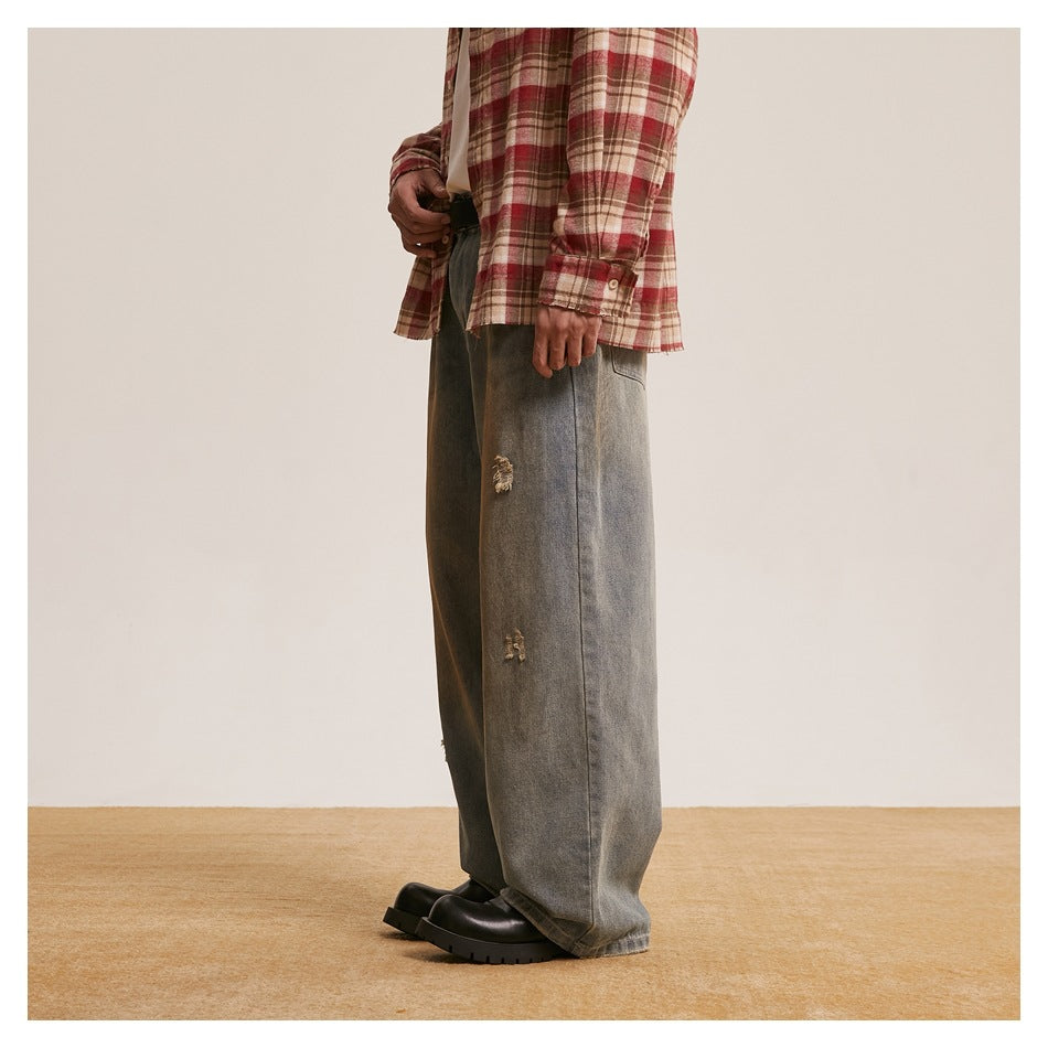 Side view of a model wearing loose, faded gray-blue jeans with distressed patches and black chunky shoes.