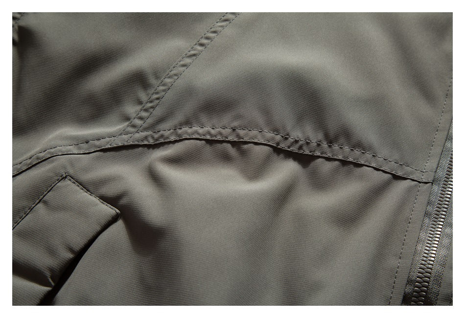Close-up of stitched panel seams and zipper on olive-gray jacket fabric.