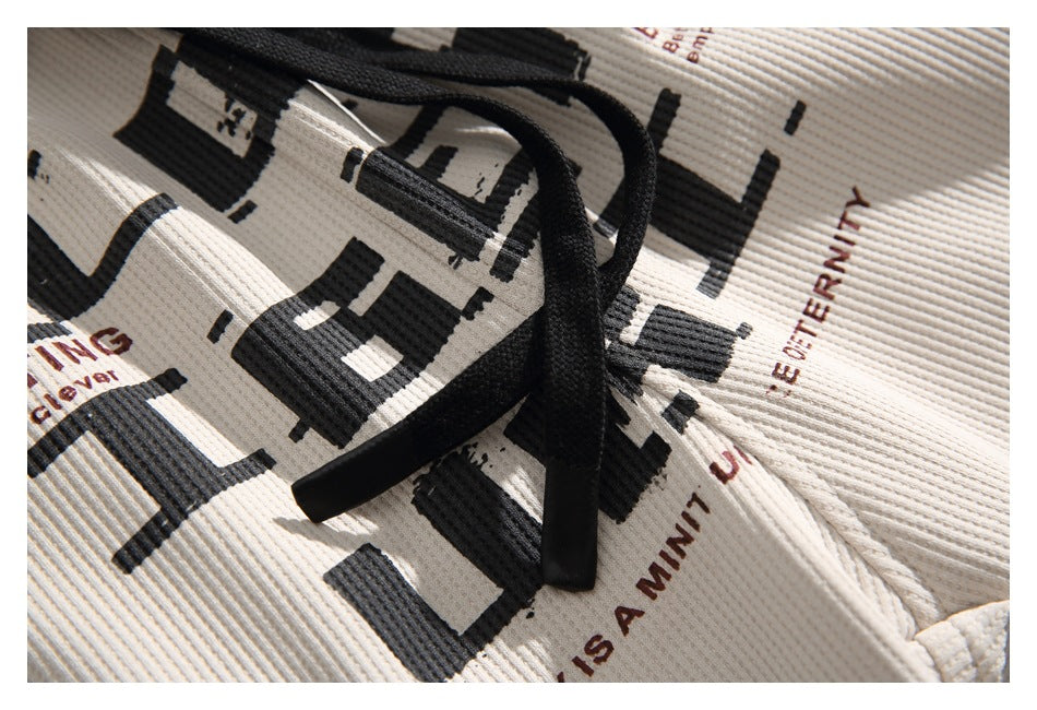 Close-up of cream ribbed garment with black drawstring and bold black and brown lettering print.