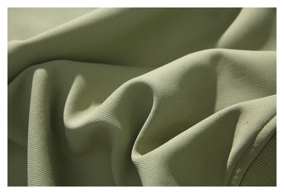 Close-up of folds in pale sage-green sweatshirt fabric, showing its surface and ribbed edge.