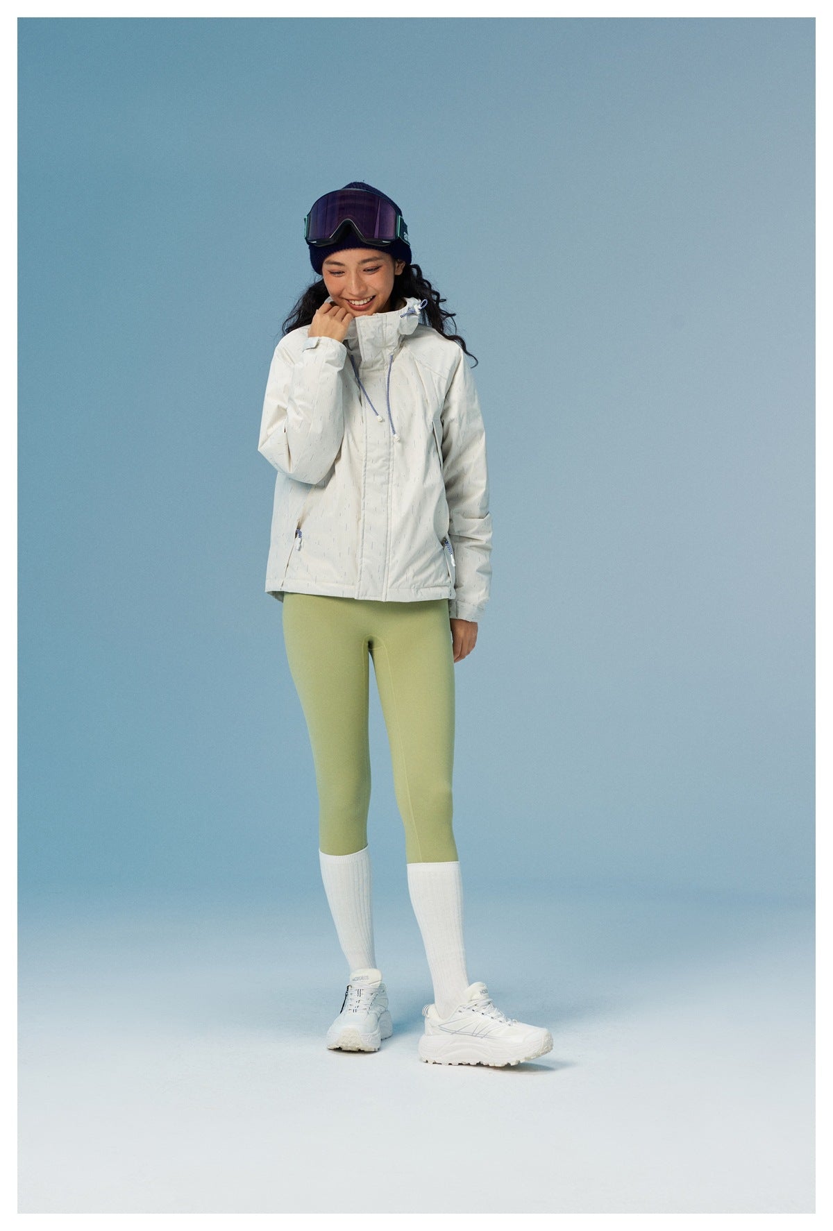 Full-length view of a woman wearing a white speckled hooded jacket and light green leggings.
