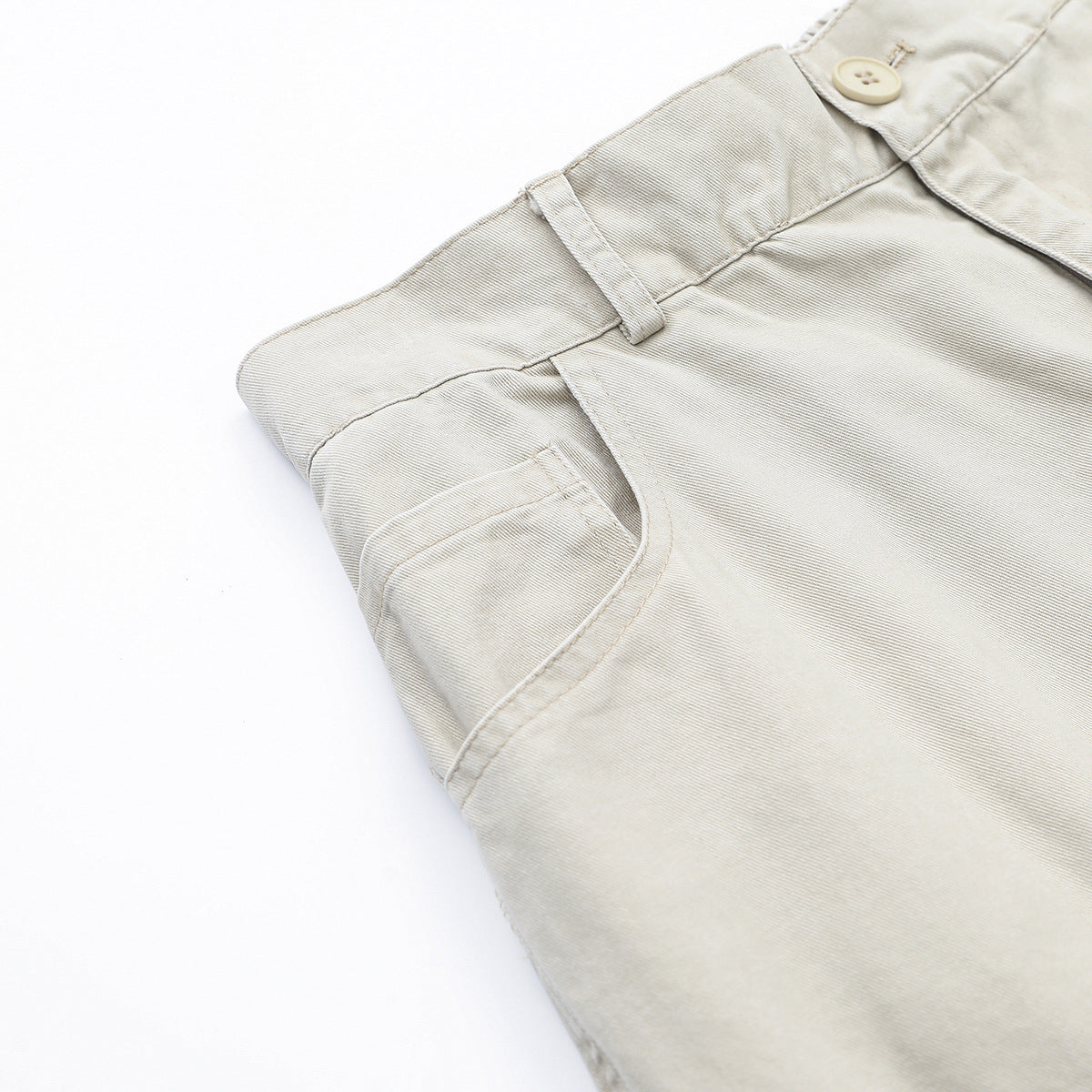 Close-up of light beige trousers showing the waistband, belt loop, button, and curved front pocket.