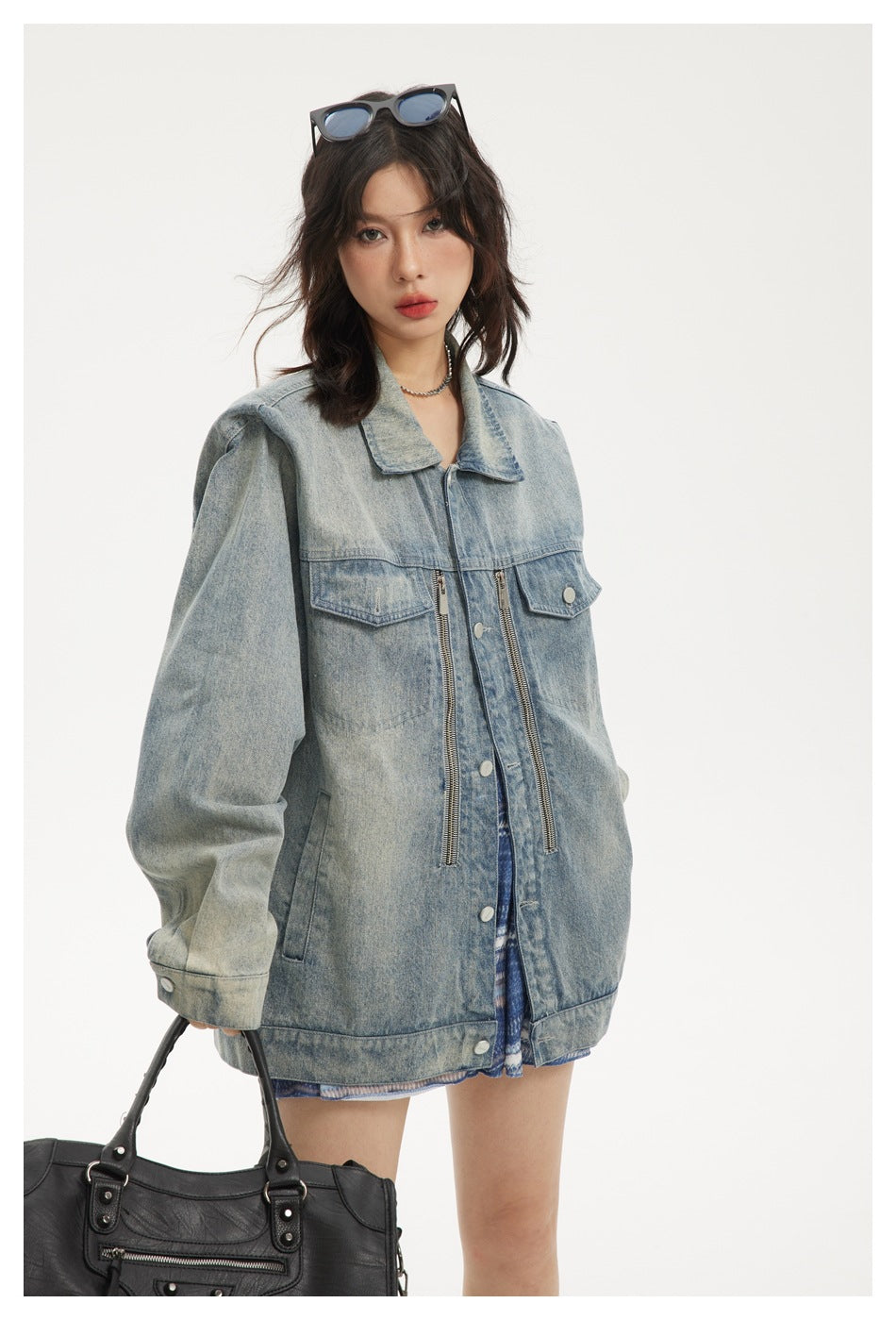 Closer view of a model wearing an oversized light-wash denim jacket with chest flaps and long front zippers.