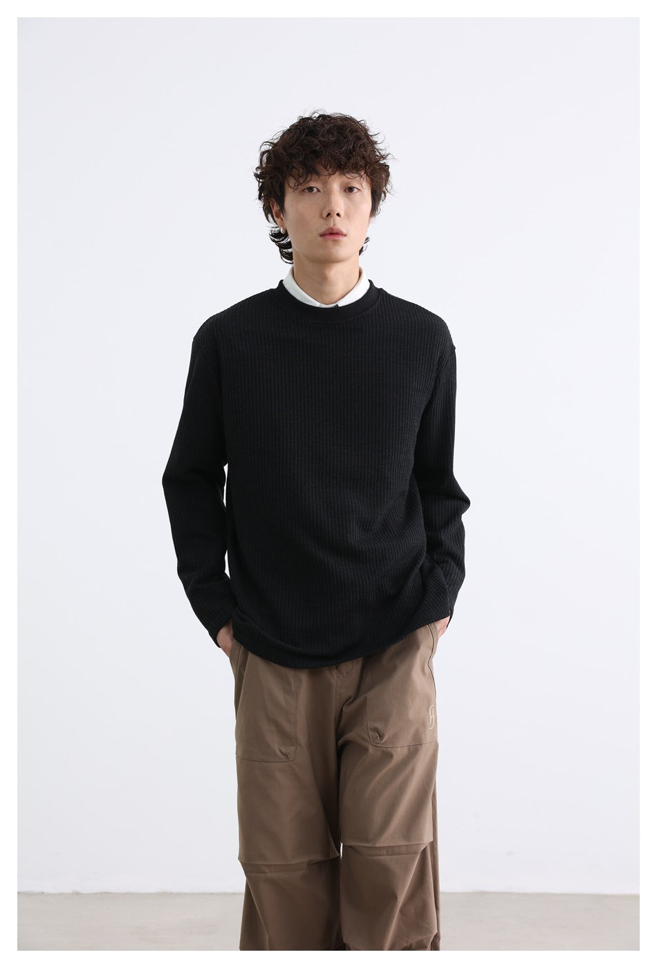 Front view of a model wearing a black ribbed long-sleeve crewneck over a white collared shirt.
