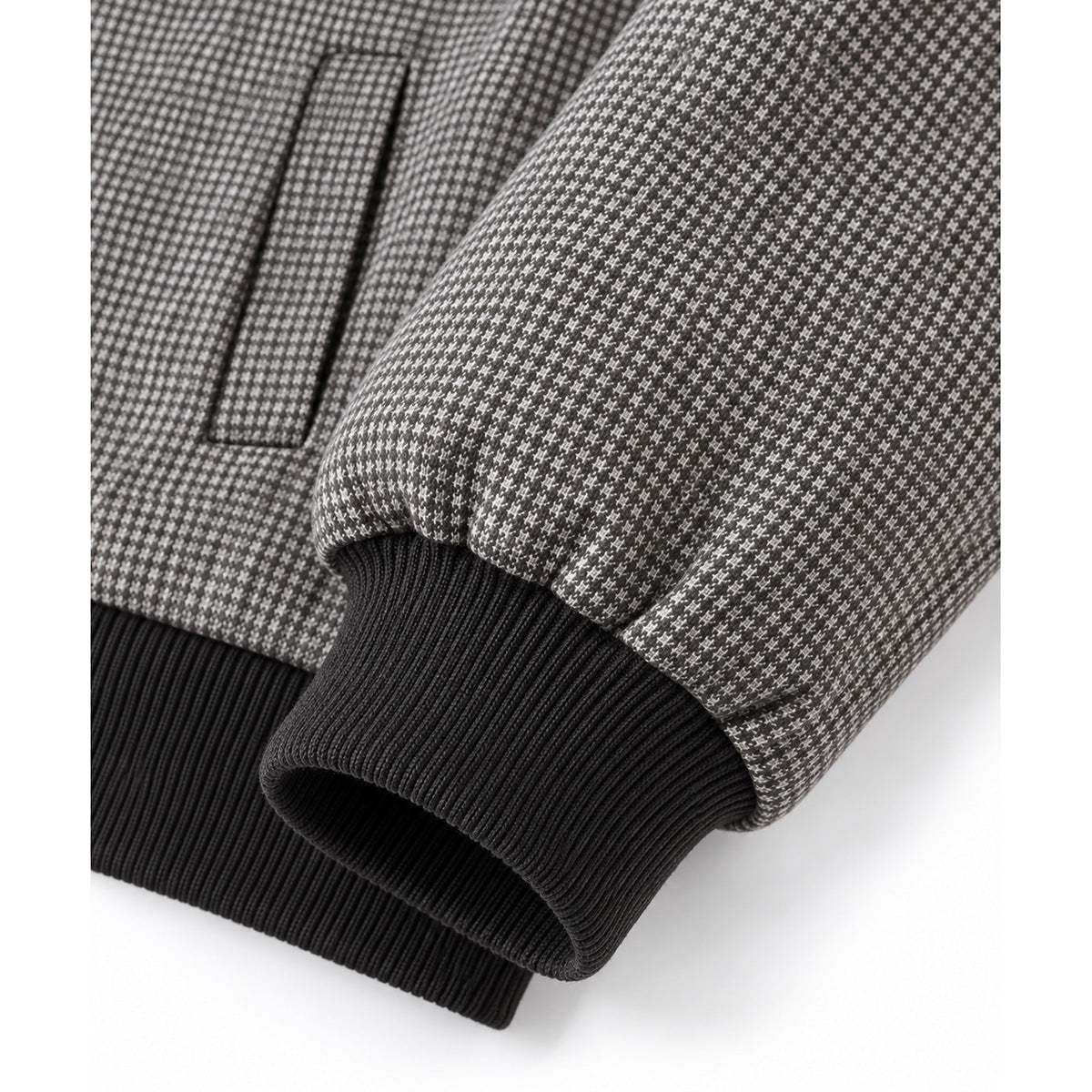 Close-up of the gray micro-patterned jacket's fabric, dark ribbed cuff and hem, and welt pocket.
