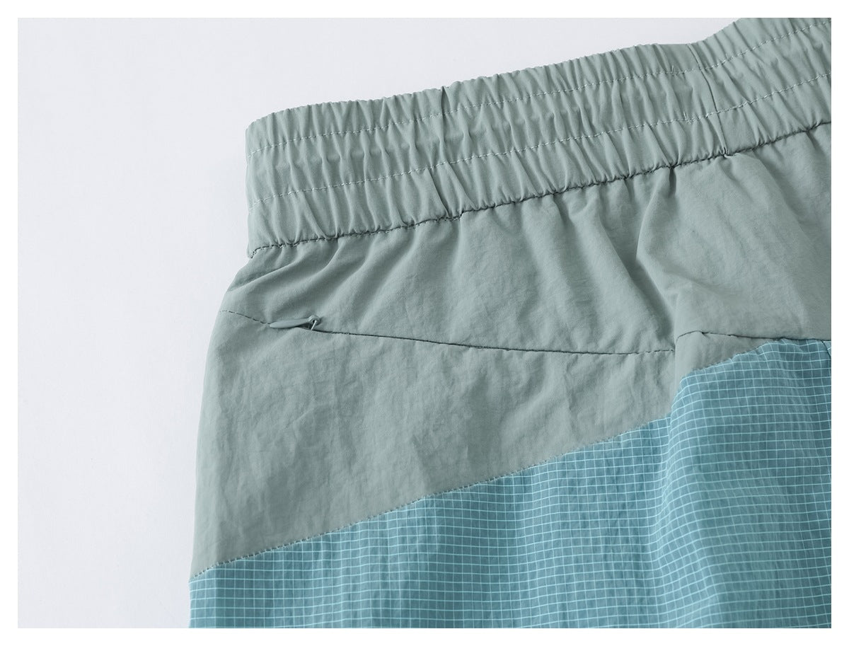 Close-up of pale sage elastic waistband and seam above a teal fine-check color-block panel.