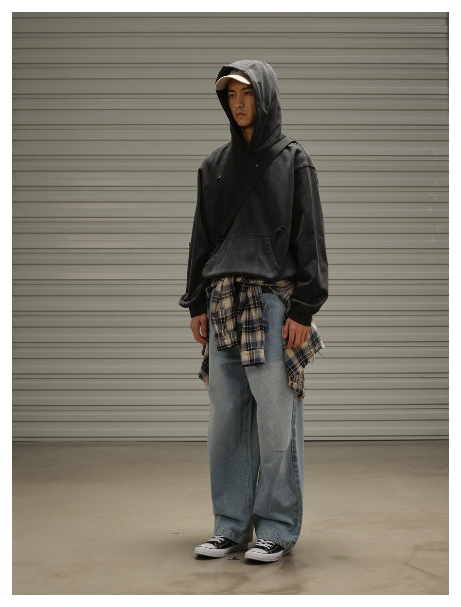 Model in a black distressed hoodie with the hood up, loose blue jeans and a plaid shirt tied at the waist.