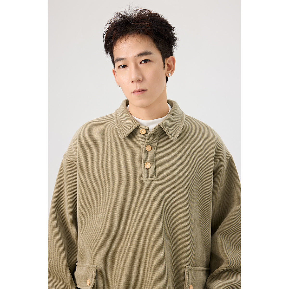 Close-up of an olive pullover showing its ribbed texture, pointed collar, three-button placket and flap pockets.