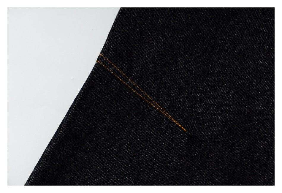 Close-up of black denim with a diagonal seam and contrasting orange stitching.