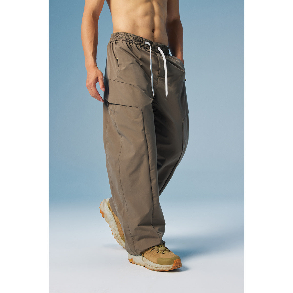 Model wearing taupe wide-leg pants with an elastic waist, white drawstrings and large layered side pockets.