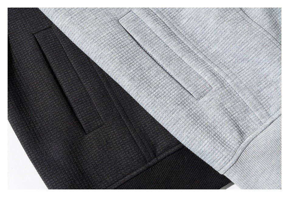 Close-up of pocket and seam details on light gray and black textured garments.