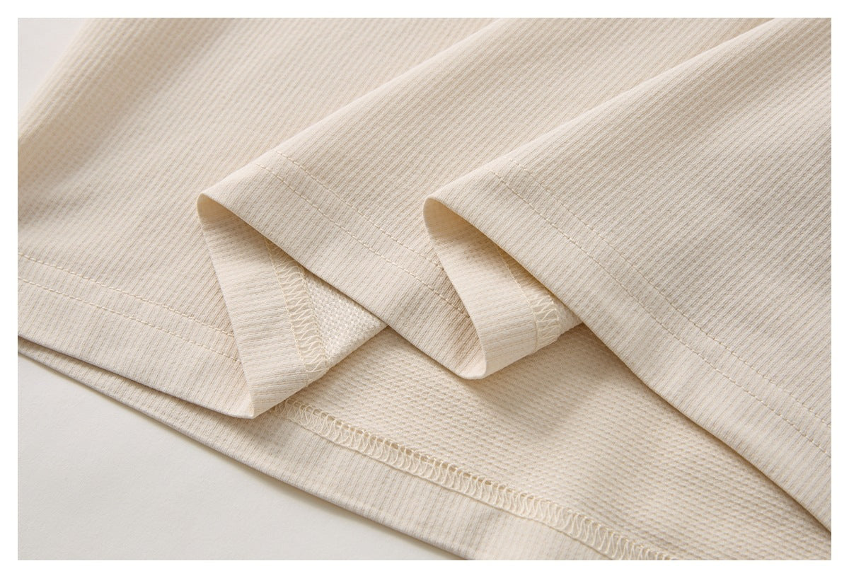 Close-up of the cream garment's folded hem and visible overlock stitching.