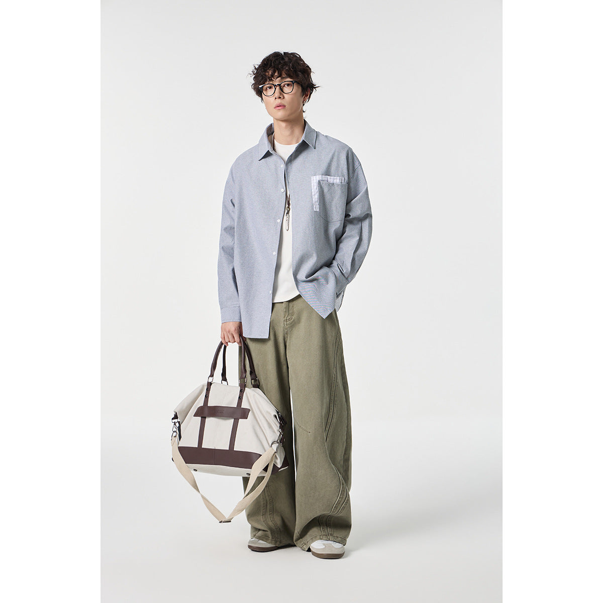 Model wearing a loose gray button-up shirt with checked chest pocket trim and olive wide-leg pants.