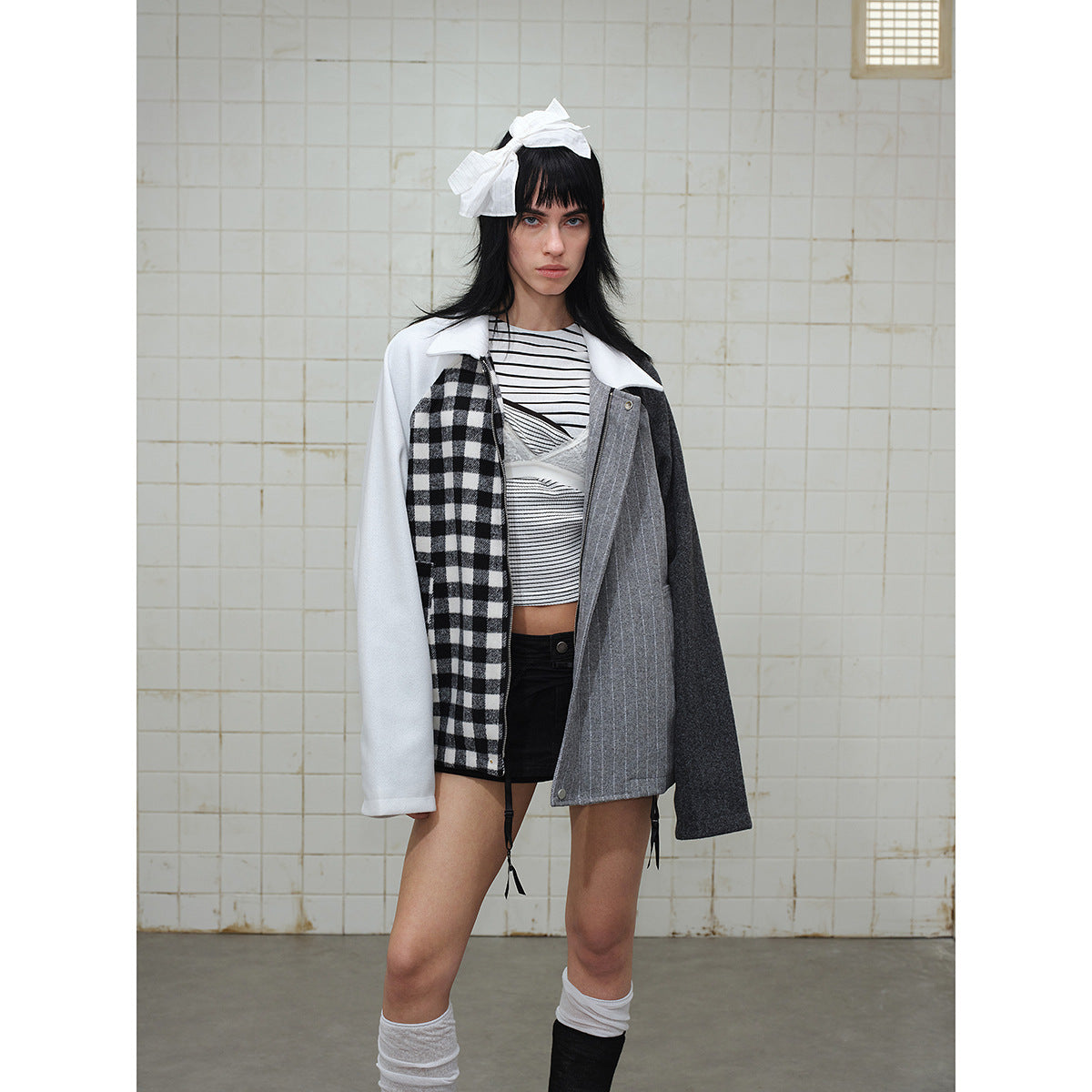 Model wearing a patchwork jacket with white sleeves, a black-and-white check panel, gray pinstripes and a dark sleeve.