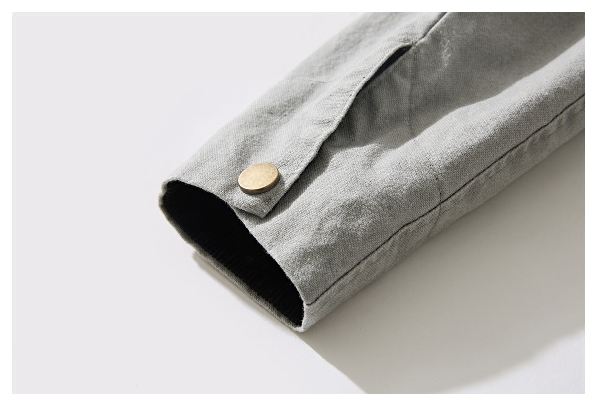Close-up of a light gray sleeve cuff with black lining and a round brass-colored snap.