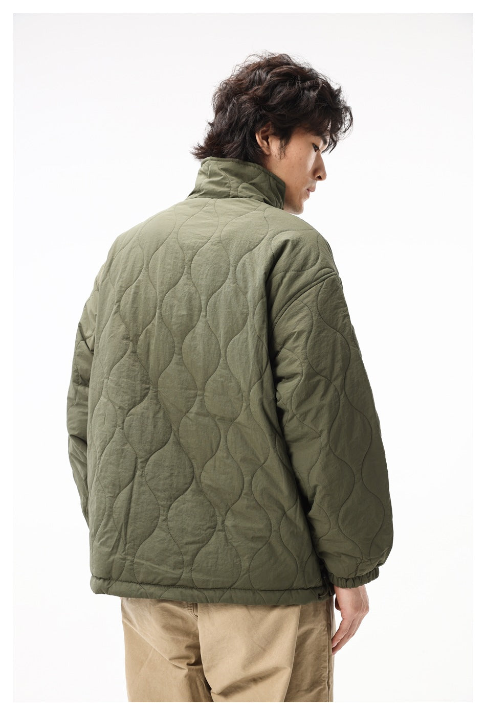 Rear view of a man wearing an olive quilted jacket with a high collar and elastic cuffs.
