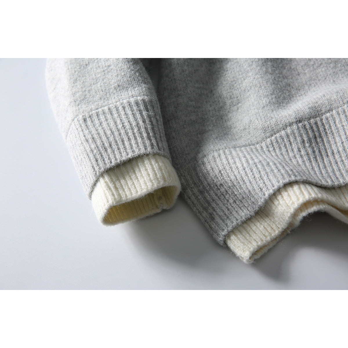 Close-up of gray ribbed cuffs and hem with cream-colored knit layers showing underneath.