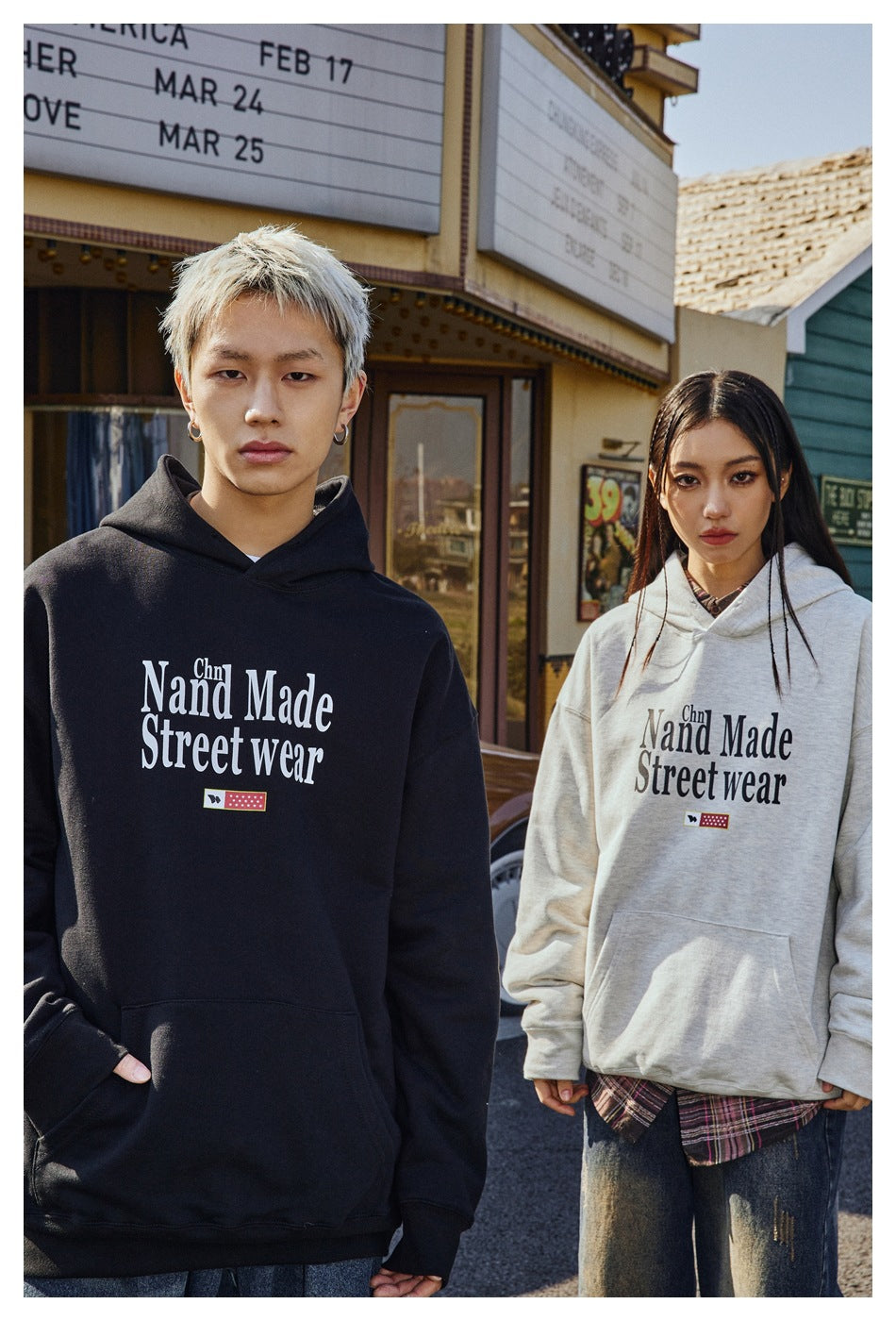 Two models pose in black and light gray pullover hoodies, showing the front lettering and kangaroo pockets.