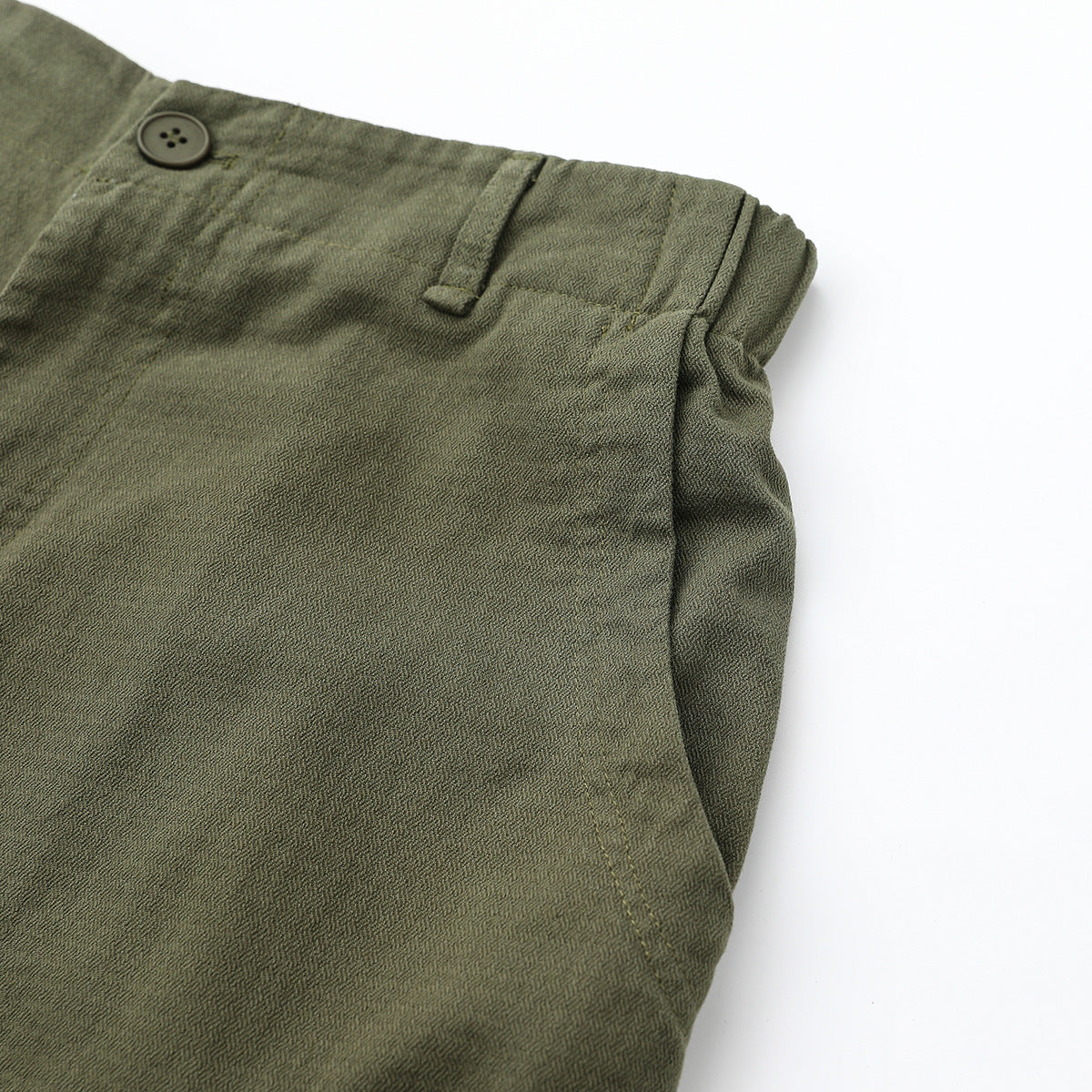 Close-up of olive-gray pants showing the waistband button, belt loop, and side pocket opening.
