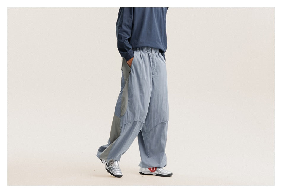 Model in profile wearing loose light blue-gray pants with pale side panels and gathered ankles.