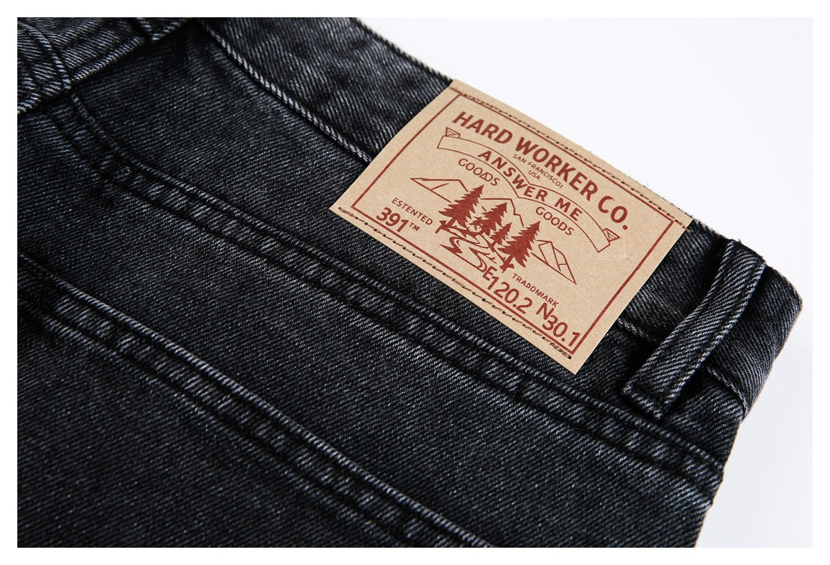 Close-up of black jeans showing the waistband, belt loop, stitching, and a tan branded patch.