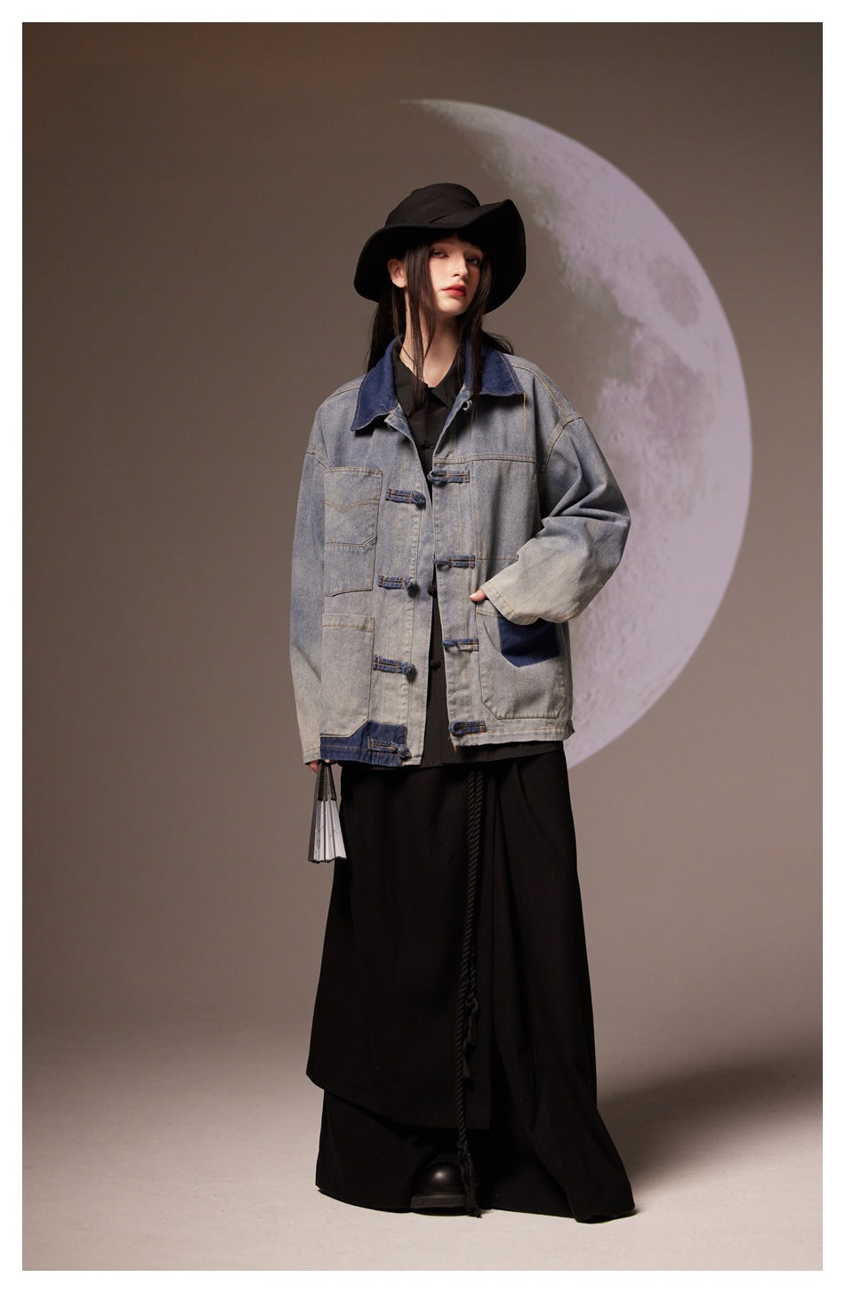Model in a gray denim jacket with dark blue details and frog closures, paired with a long black skirt.