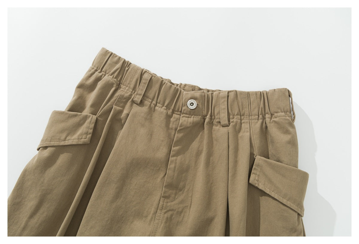 Close-up front view of khaki cargo pants showing an elastic waist, button, belt loops and flap pockets.
