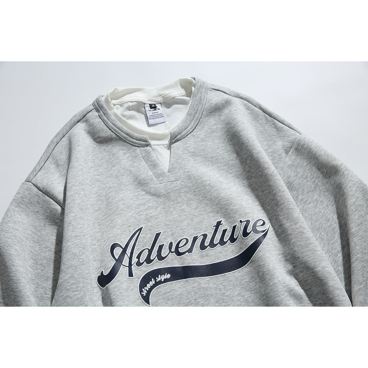 Close front view of a heather-gray sweatshirt with a white collar insert and navy “Adventure” script graphic.