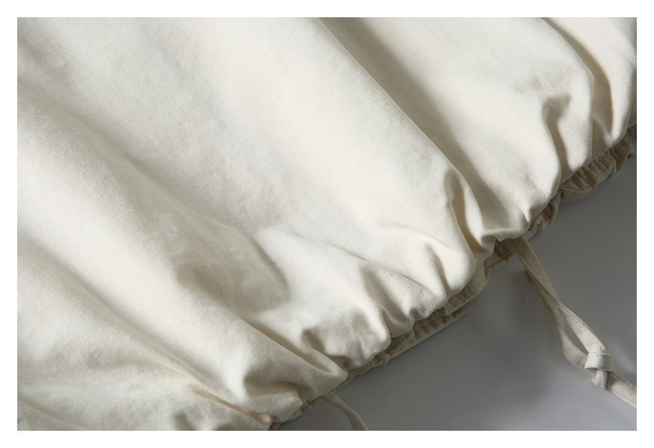 Close-up of an ivory garment’s gathered edge with narrow fabric drawstrings.