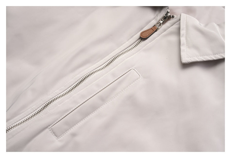 Close-up of a pale gray jacket's silver zipper, brown pull tab, and narrow welt pocket.