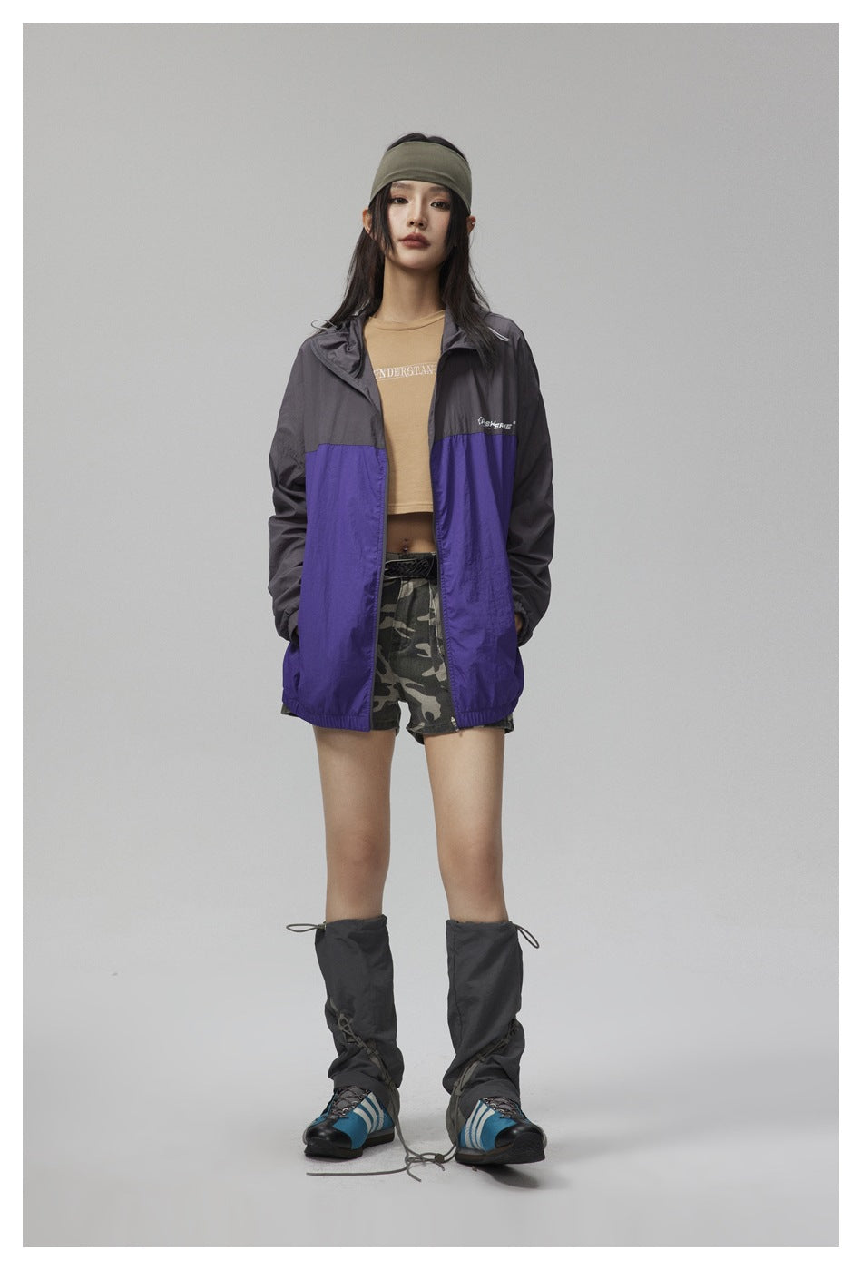 Model wearing the charcoal and purple hooded zip jacket open over a tan cropped top and camouflage shorts, front view