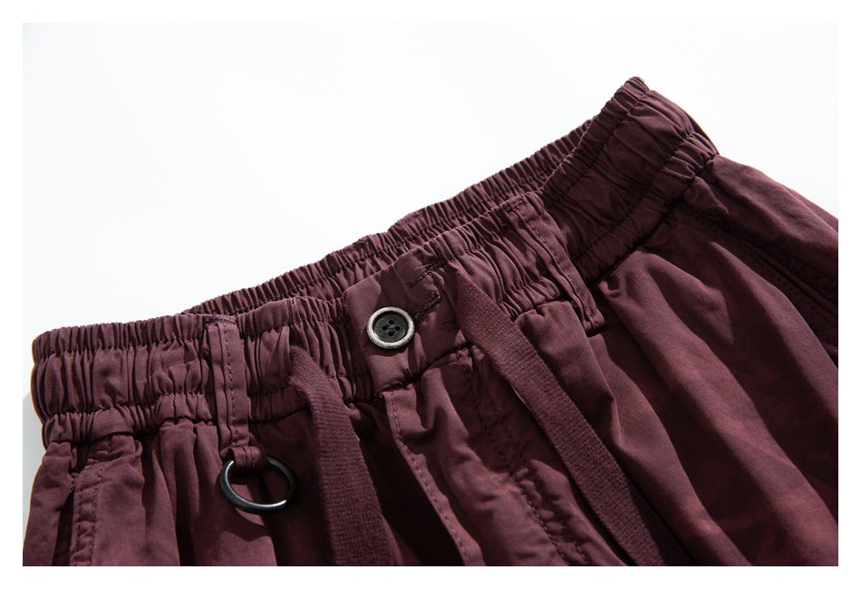 Close-up of burgundy pants with an elastic waistband, button, drawstring, and metal ring.