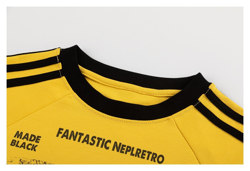 Close-up of the yellow T-shirt's black crew neck, striped shoulders, and printed chest lettering.