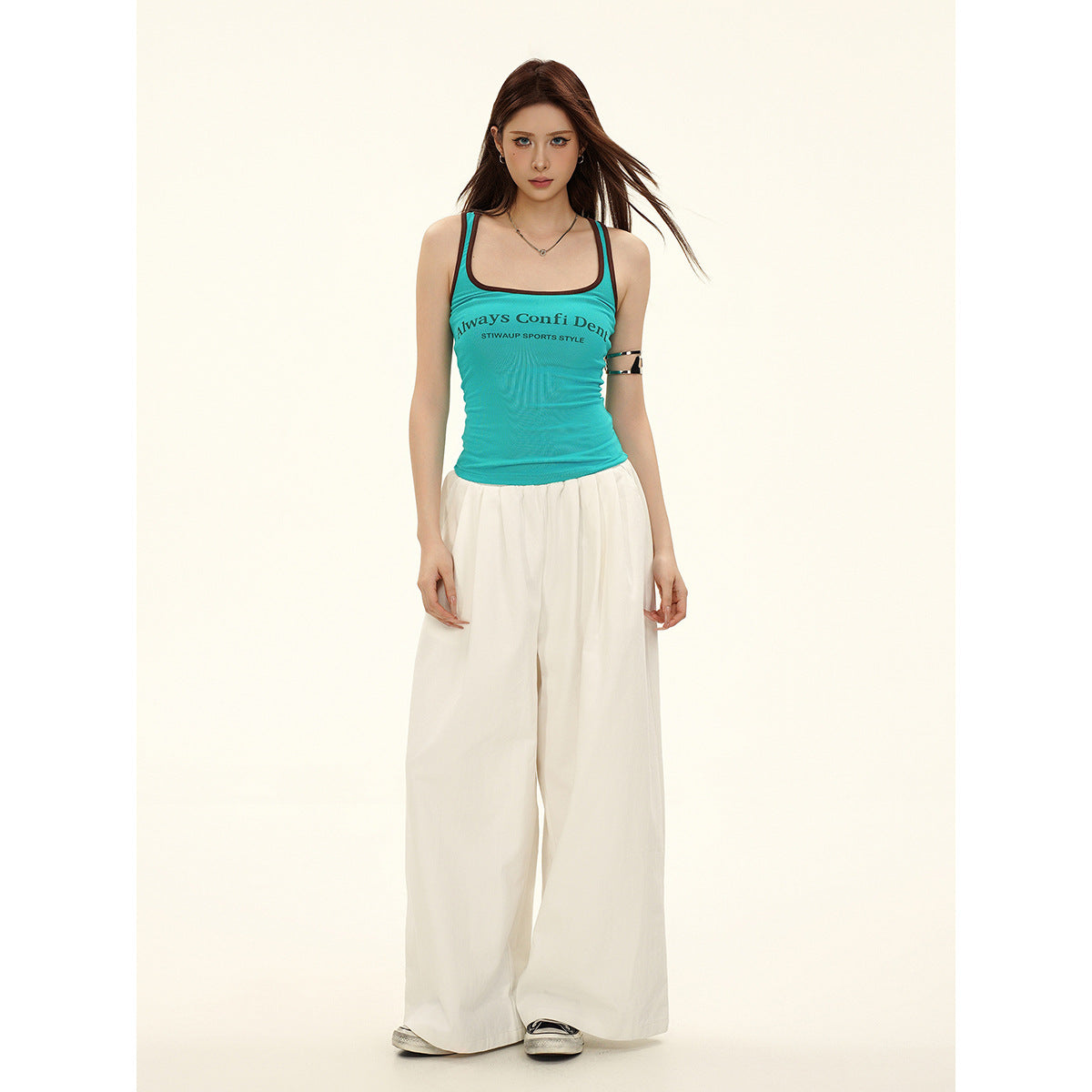 Model wearing a turquoise racerback tank with dark trim and white wide-leg pants, full-length front view.