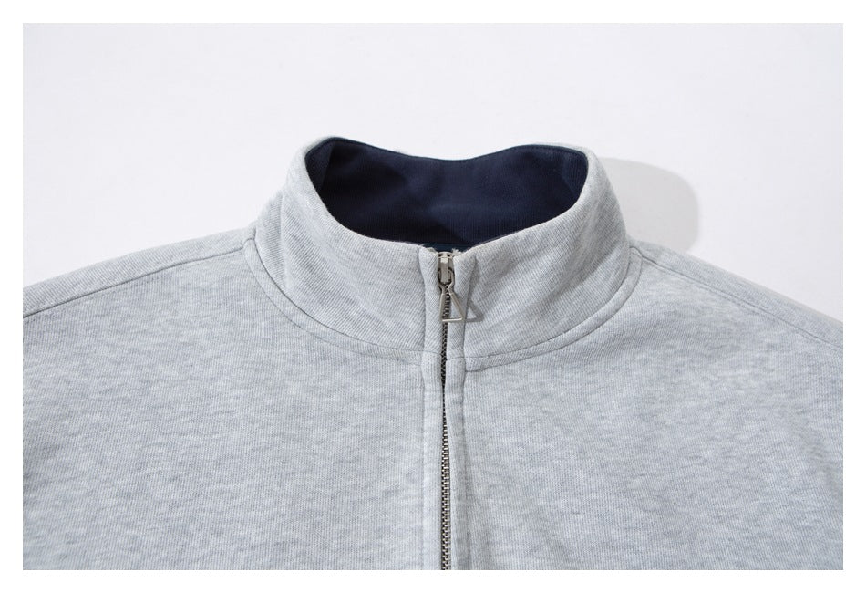 Close-up of a light gray zip-up jacket's raised collar, dark lining, and metal zipper.